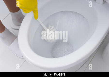Housewife cleaning the toilet in the bathroom using a toilet brush and antibacterial detergent, close up view of the toilet bowl Stock Photo