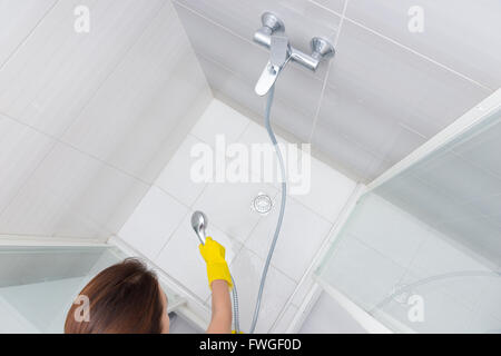 Housekeeper rinsing the white tiles on a shower cubicle as she attends to the daily cleaning of the bathroom, view from above Stock Photo