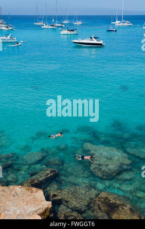 Two people do snorkeling near the rocks and boats in a wonderful blue and green sea Stock Photo