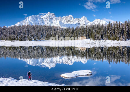 Hiker admires the snowy peaks and woods reflected in Lake Palu, Malenco Valley, Valtellina, Lombardy, Italy, Europe Stock Photo