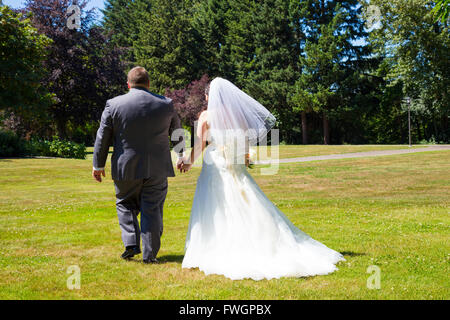 A bride and groom walk away from the camera holding hands at this outdoor wedding venue location in a park after just tying the  Stock Photo
