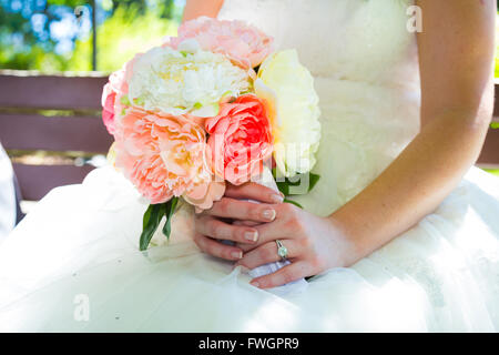 This bride holds her bouquet of white and pink flowers against her white wedding dress. Stock Photo