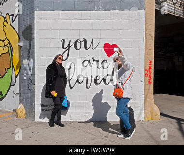 Tourists taking selfies in front of a 'You Are Loved' wall on Kenmare St. corner of Mulberry in NOLITA, Manhattan New York City. Stock Photo