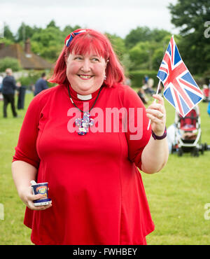 Church of England curate wearing a red gown and waving a Union Jack flag during the Queen's 90th Birthday celebrations in the New Forest town of Fordingbridge, Hampshire, UK Stock Photo