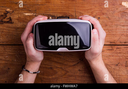 Hands of man holding virtual reality goggles, wooden table Stock Photo