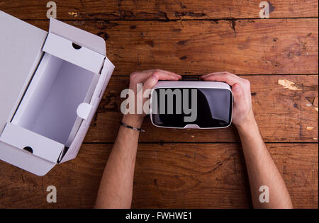 Hands of man holding virtual reality goggles, wooden table Stock Photo