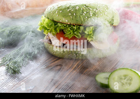 burger with green bun in light smoke on wooden background. Stock Photo