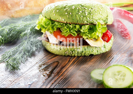burger with green bun in light smoke on wooden background. Stock Photo