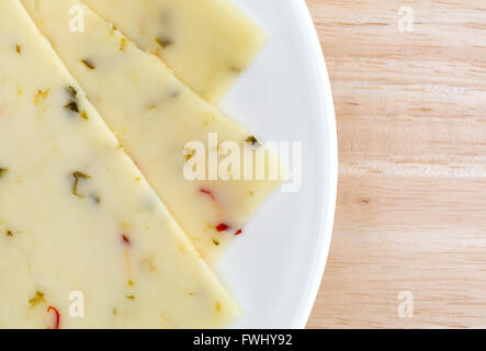 Top close view of pepper jack cheese slices on a white plate atop a wood table top. Stock Photo