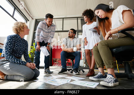 Group of young creative team going over some plans together. Documents laid out on floor with finalizing the design. Stock Photo