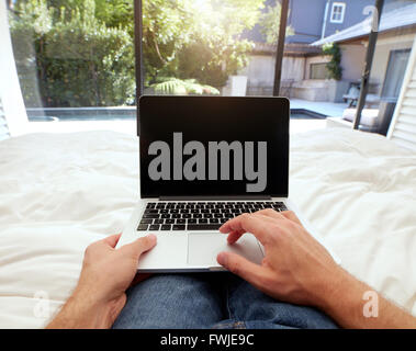 Closeup image of man lying on a bed working on laptop computer. POV shot of man relaxing in bedroom using touch screen computer. Stock Photo