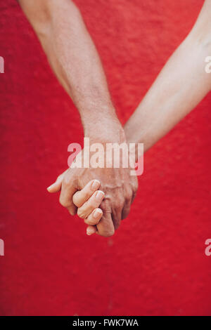Close up of mature couple holding hands against red wall. Vertical shot of loving man and woman holding hands. Stock Photo