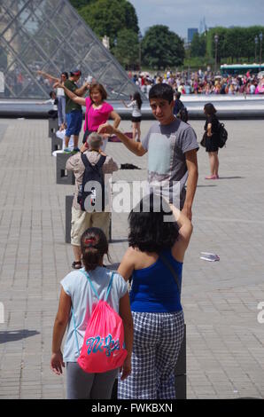 Tourists standing in a  row and posing to take a picture where they touch the top of Louvre pyramid in Paris Stock Photo