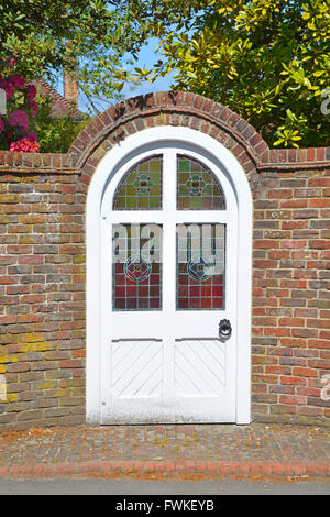 Brick arch round top door with stained glass window panes external brick garden boundary wall opens directly onto public pavement Lyndhurst England UK Stock Photo