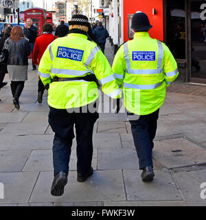 Back view WPC female Metropolitan Police officer in distinctive cap (left) & male officer traditional helmet patrolling London West End England UK Stock Photo