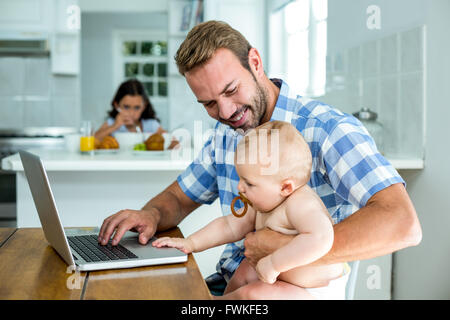 Father looking at baby boy while using laptop at home Stock Photo