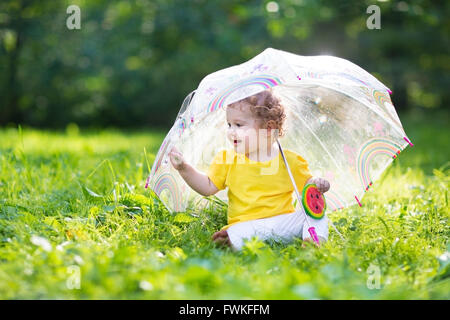 Little girl with colorful umbrella playing in the rain. Kids play outdoors by rainy weather in fall. Stock Photo