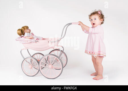 Funny baby girl walking with a doll stroller Stock Photo