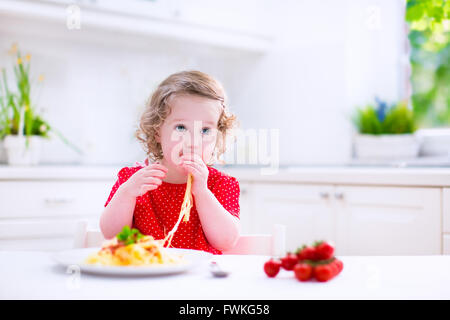 Kids eat pasta. Healthy lunch for children. Toddler kid eating spaghetti Bolognese in a white kitchen at home. Stock Photo