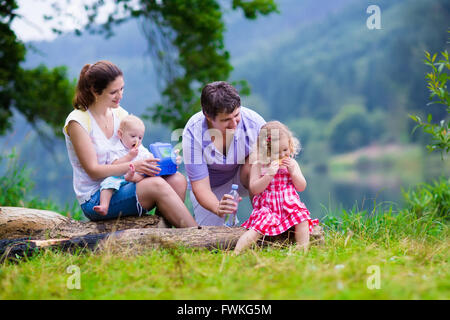 Family on summer hike. Young parents with kids hiking next to a lake. Mother, father and two children having picnic outdoors Stock Photo