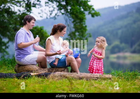 Family on summer hike. Young parents with kids hiking next to a lake. Mother, father and two children having picnic outdoors Stock Photo