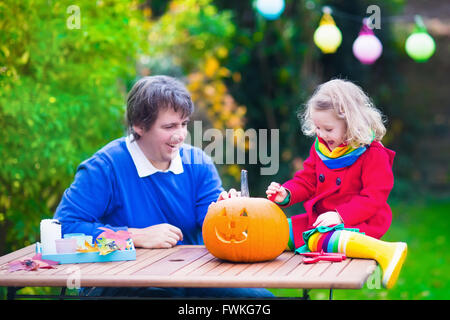 Family carving pumpkin at Halloween. Dressed up child trick or treating. Kids and parents trick or treat. Child in witch costume Stock Photo