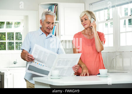 Senior man reading newspaper while woman using phone Stock Photo
