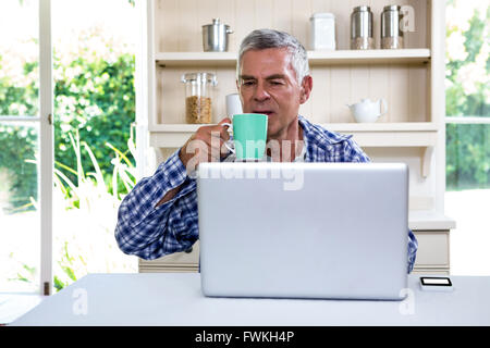 Senior man drinking coffee while using laptop Stock Photo