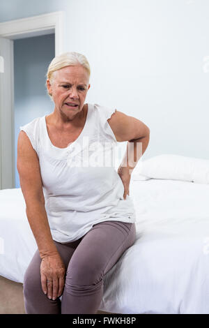 Senior woman suffering from back pain while sitting in bedroom Stock Photo