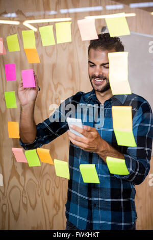 Man using mobile phone while writing on sticky notes Stock Photo