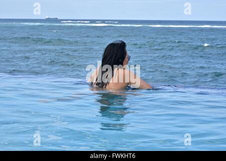 A woman in an infinity pool overlooking the ocean in Puerto Rico Stock Photo