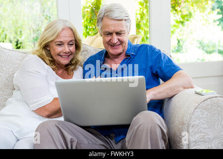 Exited senior couple using laptop while sitting in living room at home Stock Photo