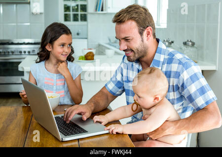 Happy father using laptop while taking care of children Stock Photo