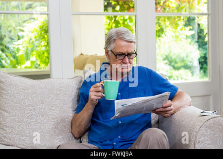 Senior man reading newspaper while having coffee at home Stock Photo