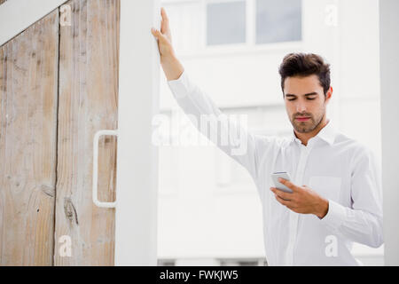 A businessman is looking his smartphone and posing his hand on a wall Stock Photo