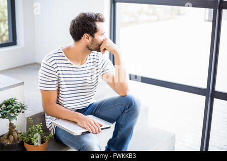 Man sitting with laptop looking out through window Stock Photo