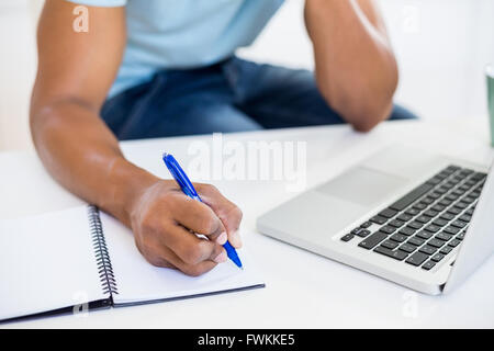 Mid section of a man with laptop writing in diary Stock Photo