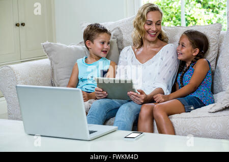 Mother sitting with daughter and son using tablet on sofa Stock Photo