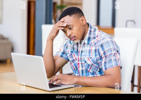 Tense young man using laptop in kitchen Stock Photo
