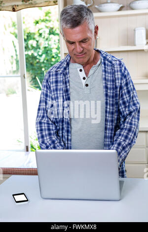 Senior man using laptop in kitchen Stock Photo
