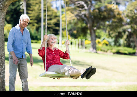 Senior man pushing his partner on swing Stock Photo