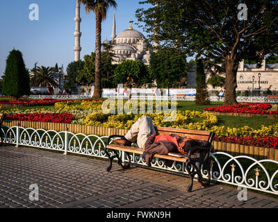 Homeless man sleeping in morning on bench in park in front of the Blue Mosque (Sultan Ahmed Mosque) in Istanbul, Turkey Stock Photo