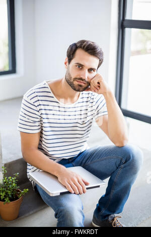 Portrait of thoughtful man sitting on steps with laptop Stock Photo
