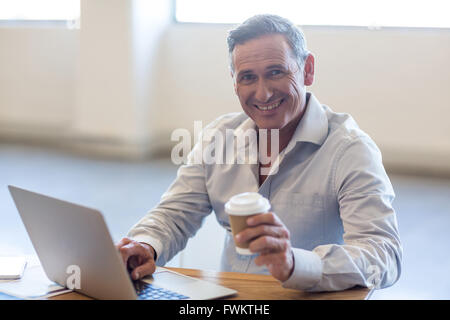 Businessman holding disposable coffee cup and using laptop Stock Photo