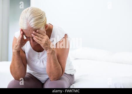 Senior woman with head in hand sitting at  bedroom Stock Photo