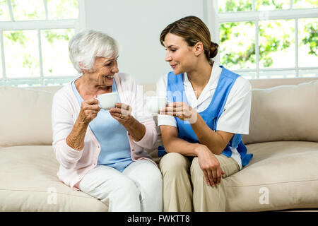 Smiling nurse and senior woman holding coffee cups