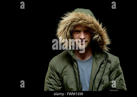 Low key studio portrait of young adult confident caucasian model wearing winter coat with hood on and smirking. Isolated on blac Stock Photo