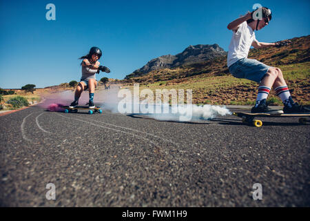 Young man and woman practicing skating on skateboard with smoke grenade. Teenagers longboarding on open road. Skate board with s Stock Photo