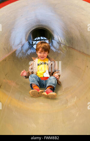 Young boy has fun going down a slide hole Stock Photo