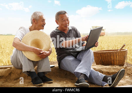 Two farmers sitting in field talking Stock Photo